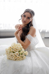 Elegant bride posing with bouquet in bright indoor setting before wedding ceremony