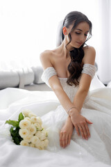 Bride in elegant white gown poses gracefully with bouquet in a bright indoor setting