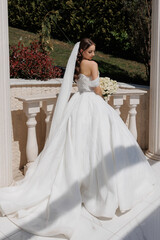 Elegant bride stands gracefully on balcony wearing a stunning white gown near greenery