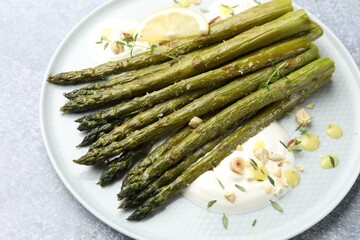 Tasty cooked asparagus served with lemon and sauce on grey table, closeup
