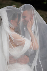 Couple embraces under a romantic veil during their wedding ceremony in a serene outdoor setting