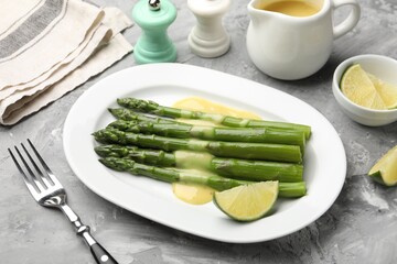 Tasty cooked asparagus served with sauce and lime on grey textured table, closeup