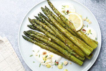 Tasty cooked asparagus served with lemon and sauce on grey table, top view