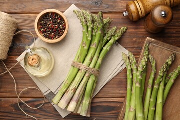 Fresh raw asparagus, spices and oil on wooden table, flat lay
