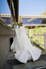 Bride in elegant wedding gown ascending stairs on sunny day at contemporary venue