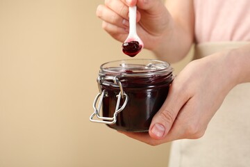 Woman with tasty cherry jam on beige background, closeup. Space for text