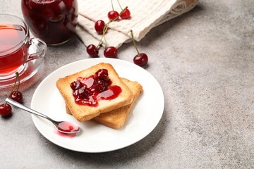 Toasts with tasty cherry jam, tea and fresh fruits on grey table. Space for text