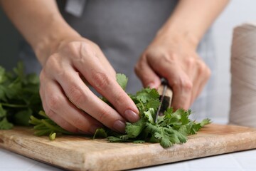 Woman cutting fresh cilantro at white table, closeup