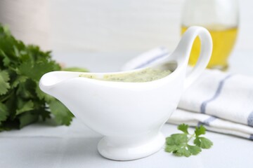 Tasty cilantro sauce in gravy boat on light tiled table, closeup