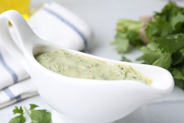 Tasty cilantro sauce in gravy boat on light table, closeup
