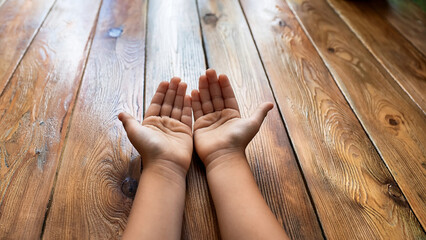 Open hands of a child raised in prayer or request gesture on wooden surface. Concept of spirituality, innocence, faith, or hope in childhood. Top view with natural lighting and warm tones.