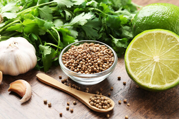 Fresh cilantro, coriander seeds, lime and garlic on wooden table, closeup