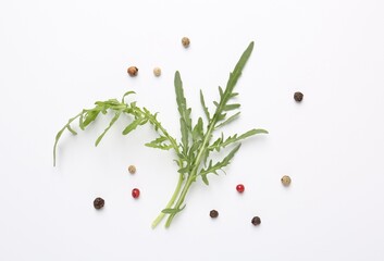 Fresh ripe green arugula leaves and peppercorns on white background, flat lay