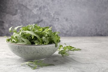 Fresh ripe green arugula leaves in bowl on grey table, closeup. Space for text