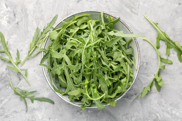 Fresh ripe green arugula leaves in bowl on grey table, flat lay