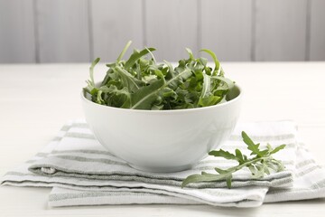 Fresh ripe green arugula leaves in bowl on white wooden table, closeup
