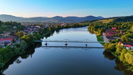 Approaching a footbridge crossing the narrow river crossing the village. Sunset view of the countryside in Slovakia. Tatra mountains at backdrop.