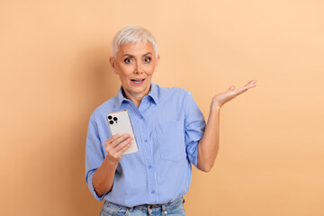 Senior woman with short white hair using a smartphone while gesturing against a beige background