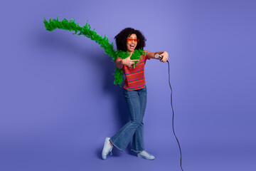 Young woman with microphone wearing sunglasses and feather boa striking a playful pose against a...