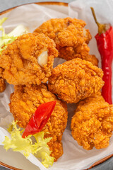 Crispy golden fried chicken pieces served on parchment paper with red chili pepper and fresh lettuce garnish