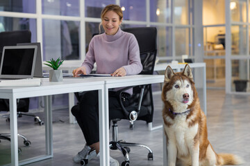 Blonde young woman sitting at the table, a big dog sitting near