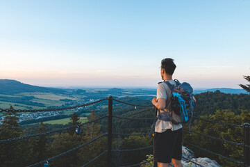 Backpacker stands on a platform at golden hour, overlooking the forested hills and valleys of the...