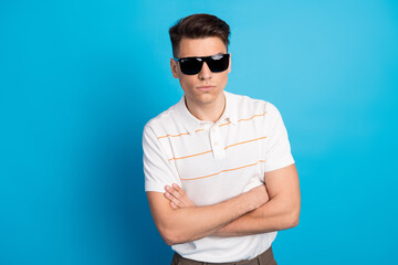 Confident young man wearing sunglasses and white polo shirt against a vibrant blue background,...