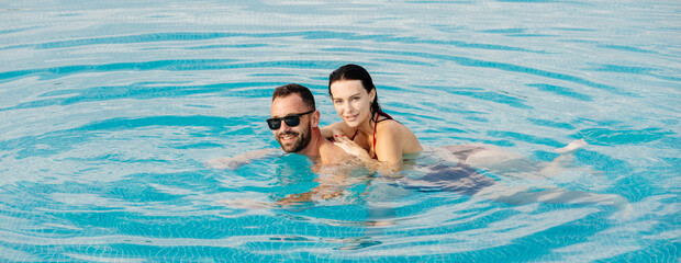 Happy young couple swimming in a pool on a sunny summer day, enjoying each other’s company. Concept vacation, intimacy, summer vibes.