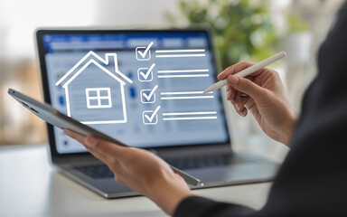 Digital home assessment person using laptop and tablet with a house icon and checklist on screen for real estate or property evaluation