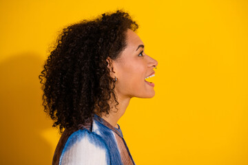 Side profile of a cheerful young woman with curly hair, dressed in a casual outfit, standing...