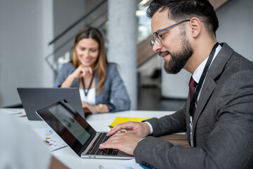 Businessman working on laptop with charts and graphs, analyzing financial data with female colleague in office