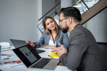 Business colleagues discussing charts on laptop in modern office