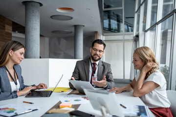 Business team discussing financial results using digital tablet and laptop in modern office