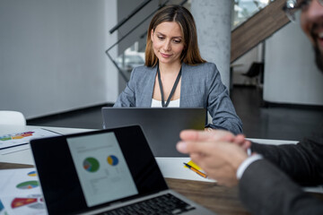 Businesswoman working on laptop with charts and graphs, discussing with colleague