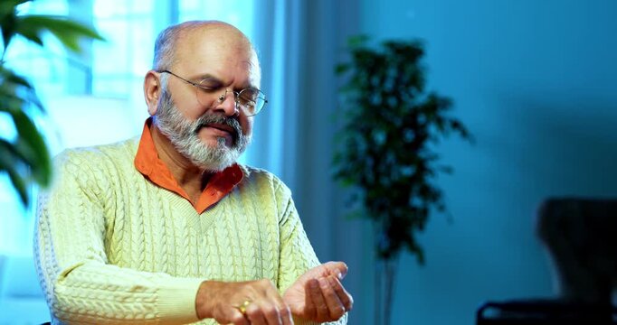 Indian senior man checking sugar level at home using handheld glucometer device, appearing sad after seeing abnormal reading, calling someone worriedly on smartphone to share health concerns
