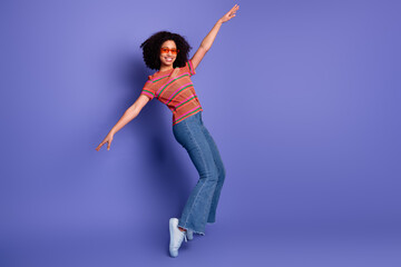 Joyful young woman posing in casual outfit with afro hair against a purple backdrop for fashion and...