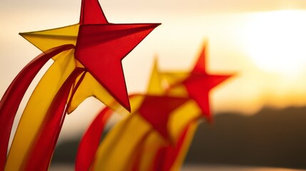 Red and yellow star-shaped lanterns glow against a golden sunset, with delicate silk ribbons fluttering in the breeze.

