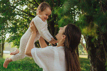 Happy young mother playing with her baby on the grass in a sunny park. Family bonding, early...