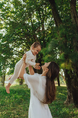 Happy young mother playing with her baby on the grass in a sunny park. Family bonding, early...