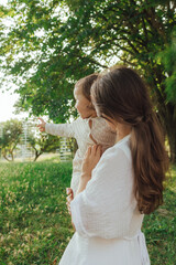 Happy young mother playing with her baby on the grass in a sunny park. Family bonding, early...