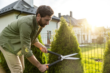 Young caucasian man cutting bushes with a prune in the garden