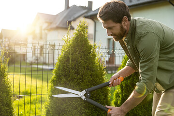 Young caucasian man cutting bushes with a prune in the garden