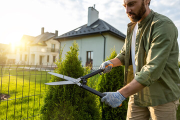 Young caucasian man cutting bushes with a prune in the garden