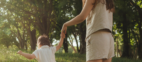 Happy young mother playing with her baby on the grass in a sunny park. Family bonding, early...