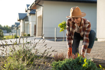 Cute young woman in straw hat planting the flowers in her garden