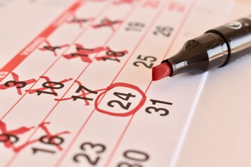 Calendar with crossed-out dates and one circled day, next to a marker. Concept of countdown,...