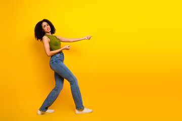 Young woman with curly hair in casual green and jeans posing against a vibrant yellow background in...