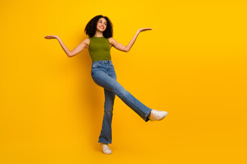 Young woman in stylish green top and jeans posing confidently on vibrant yellow background,...