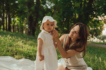Happy young mother playing with her baby on the grass in a sunny park. Family bonding, early...