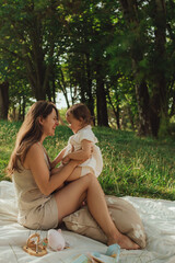 Fototapeta premium Happy young mother playing with her baby on the grass in a sunny park. Family bonding, early learning, parenting, love, outdoor lifestyle, childhood development, authentic real life moment. 